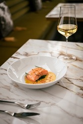 Wine pairing the poached salmon with white wine. On a fancy fine dining restaurant table.