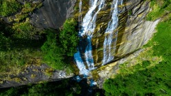 Wide aerial view of waterfall flowing in the depths of the forest. Beautifu large waterfall in the forest. Natural landscape, deep green forest and plants surrounded. Water flow from stones.