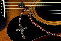 Brass crucifix and wooden rosary beads on a mahogany acoustic guitar top