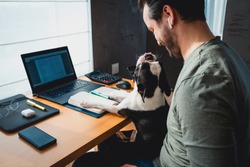 Freelancer man working from home with his dog sitting together in the office.Side view of man using laptop at home with cute dog