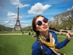  Cheerful smiling woman tourist at Eiffel Tower smiling and making travel selfie. Beautiful European girl enjoying vacation in Paris, France