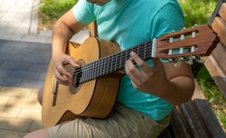 The young man plays hands and on a classic acoustic wooden guitar on the street. Focus close-up shot of teenage boy hand playing strings of an acoustic guitar.