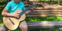The young man plays hands and on a classic acoustic wooden guitar on the street. Focus close-up shot of teenage boy hand playing strings of an acoustic guitar. High quality 4k footage