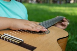 The guitarist's hand lies on the strings of a classical acoustic wooden guitar