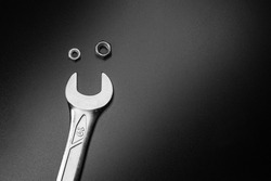 Two metal nuts and a spanner which creates a small funny smile face. Metal composition on the black table. Space for text. Background picture. Black and white.