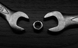 Two spanners are trying to eat a small nut, but she doesn't want to be eaten, not today. Small metal composition on the wooden table. Background picture. Black and white.
