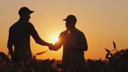 Two farmers talk on the field, then shake hands. Use a tablet