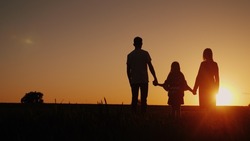 Young family with a child admiring the sunset in the field, holding hands