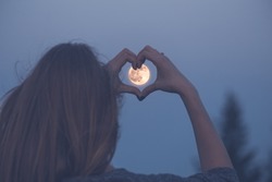 Woman making heart shape with her hands over full moon.