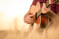 Close up of male hands playing acoustic guitar on the wheat field at the sunset. Retro, music, lifestyle concepts.
