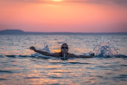 Silhouette portrait of female swimmer swimming in ocean at sunset over sea. Water sport and healthy lifestyle concepts.