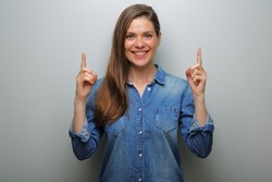 Smiling woman pointing finger up, isolated portrait on gray wall background. Wide smile with teeth.