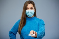 Woman wearing blue medical mask showing thermometer. Health and medical isolated concept portrait.