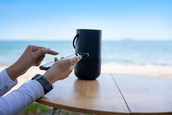 Hands connecting cell phone with bluetooth speaker with beach background, Vacation activity.