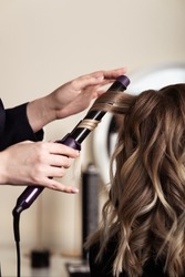 Female hands of a hair master. Close-up of blond hair on a curling iron. Curling curls. 