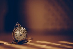 vintage pocket watch in shade lit by sun rays on blurred background
