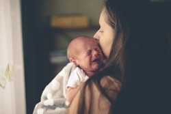 Sweet crying newborn baby at mom on hands, concept real interior, natural lifestyle photo
