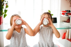 Funny grimy Children girls friends sisters in dresses drink kefir milk, yogurt in the morning in the kitchen, healthy breakfast and lactic acid foods in the children's diet.