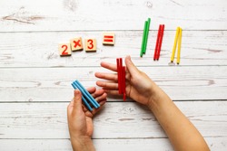 children's hands and counting material, solving examples for multiplication. Top view on a wooden table, light tone. Wooden toys and activities in elementary school