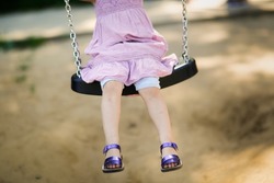 cute little toddler girl swings on swing with iron chains in park in summer, no face and legs close up