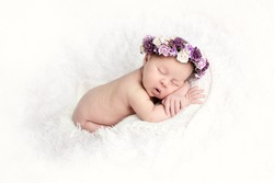 newborn sleeping baby on stomach on  light background with wreath of purple flowers, close-up, lifestyle, the concept of purity and innocence