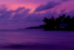 Slow speed shutter photograph of Purple evening sky with moving clouds and waves of the silhouette of cost area buildings coconut tree with a light nearby. photo taken after sunset twilight Sri Lanka