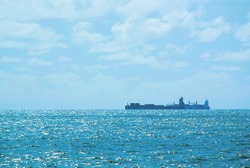 Cargo ships in the horizon line. cloudy light blue sky and blue ocean with waves. sun light reflection in sea wave edges. ships looks slightly distorted due to heat near the sea surface. 