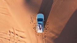 AERIAL. Top view of young couple relaxing on the car's roof at the desert.