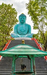 Big sitting Buddha statue, replicates the Daibutsu sculpture in Japan, situated on the top of the stairway on a mountain with a blur view of trees and a hanging lantern under the incents pavilion