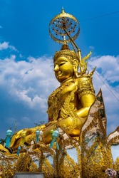 Beautiful big sitting Buddha statue decorated with traditional Thai pattern painted in gold color under the big umbrella on the top of the stairway under blue sky