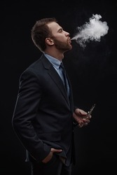 young business man blowing smoke of electronic cigarette on dark background