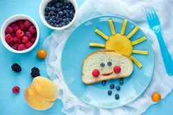 Creative breakfast idea for kids - bread bun with fruit and berry shaped funny cloud with peach sun and blueberry rain , fun with food