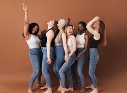 Six diverse women laughing together. Females with different body types having fun while standing against a brown background.