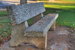 Stone Park Bench  with fallen leaves and green grass does as a high dynamic range image HDR