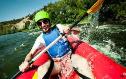 A happy entusiastic male in red inflatable canoe having a fun ride in calm waters of a river.