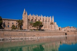 Famous beautiful gothic style La Seu Cathedral reflecting in canal water. Medieval old church against clear blue sky on sunny day. View of tourist attraction in historic town during summer.