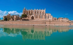 Medieval La Seu Cathedral reflecting in canal water. Gothic style church against blue sky on sunny day. Famous old tourist attraction in historic town during summer.