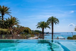 Swimming pool with view of trees and seascape. Scenic view of ocean against blue sky. Hotel spa on Mediterranean seaside during summer.