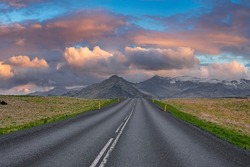 Empty diminishing road leading towards mountain. Road markings on street amidst volcanic landscape against cloudy sky. Scenic view of highway with yellow poles on roadside during sunset.