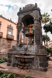 Low angle view of fountain with medieval architectural structure and old building at Plaza del Espiritu Santo in Vegueta on a cloudy day at Las Palmas, Gran Canaria, Spain