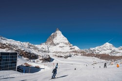 Rear view of tourist skiing on snow covered landscape and scenic view of mountain peak and clear blue sky in background during sunny day at Zermatt, Switzerland, winter holiday travel concept