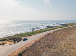 Aerial view of driving in a Ford Mustang convertible down the ocean road in California near the Pigeon Point lighthouse.