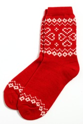 A pair of warm woolen winter socks with knitted white decorations, hearts isolated on white background. Socks for Christmas, holiday time or cold winter. Red and white color