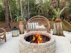 Fire pit bonfire campsite in tropical backyard woods with rustic wooden branch chairs twinkle lights lantern candles palm trees stump tables in Florida at sunset