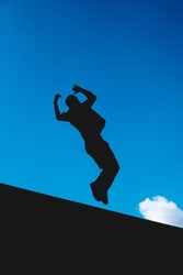 Black silhouette in the air of a man doing an extreme somersault with the sky in the background. Man training gymnastics outdoors.