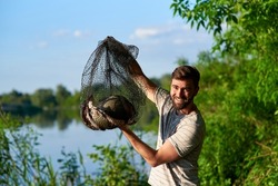 Adult fisherman holding a tank with a bog catch. Happy after a successful fishing. Sport and hobby.
