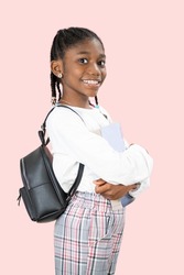 happy young 7 year old black girl student wears school backpack and holds a book in hand, isolated on pink background posing.