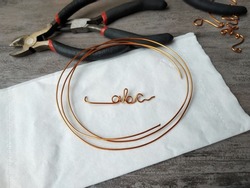 Wire alphabet. Wire writing. There are pliers and a finished piece on the table. Handmade or craft idea. 
