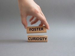 Foster curiosity symbol. Concept word Foster curiosity on wooden blocks. Beautiful grey background. Businessman hand. Business and Foster curiosity concept. Copy space. Conceptual image