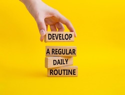 Develop a regular daily routine symbol. Concept words Develop a regular daily routine on wooden blocks. Beautiful yellow background. Businessman hand. Business concept. Copy space.